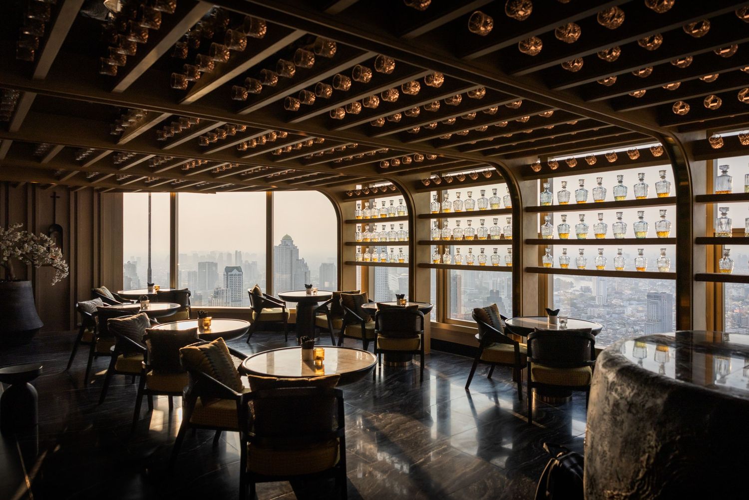 Elegant high-rise bar interior with golden ceiling lights, dark furniture, and panoramic city views.
