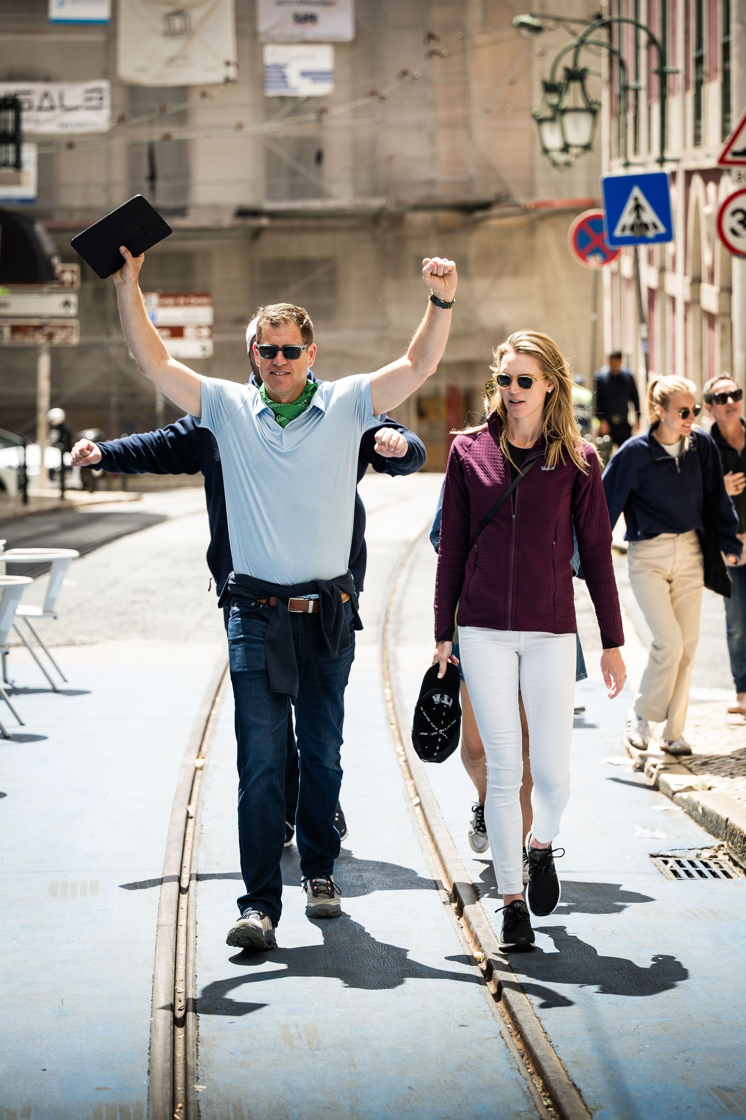 Tour guide and woman walking triumphantly along city tram tracks on sunny day.