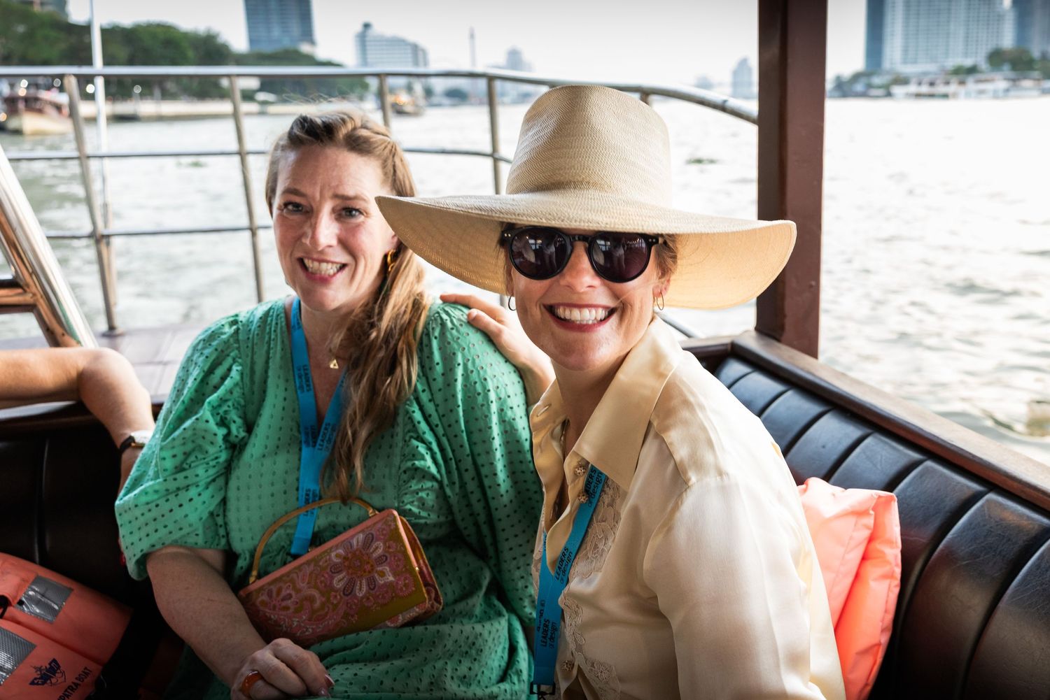 Two smiling women sitting on a boat tour along a scenic urban waterway.