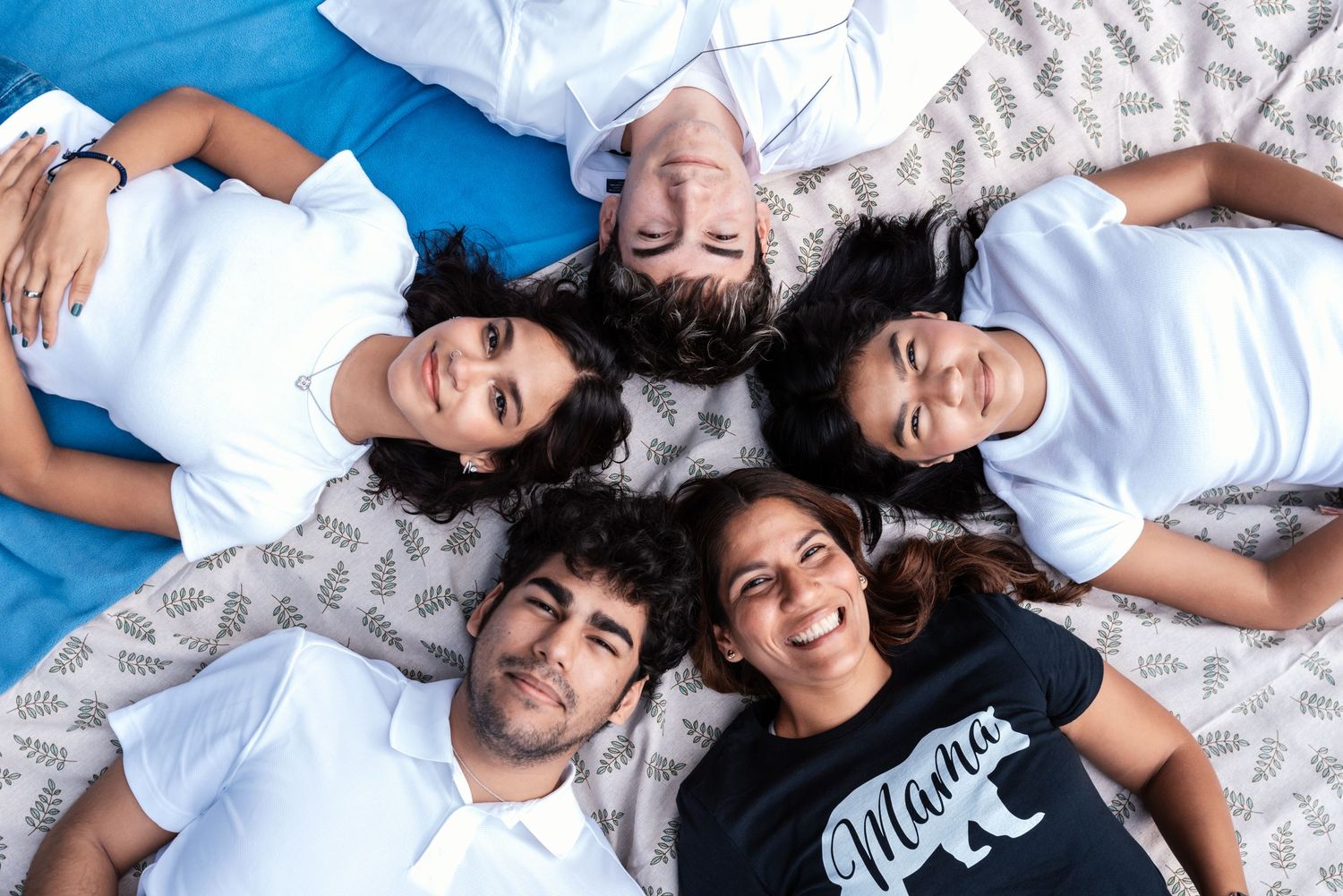 A mom with her 4 kids lies in a circle looking up at the camera and smiling during their family photo session in Nutley, NJ