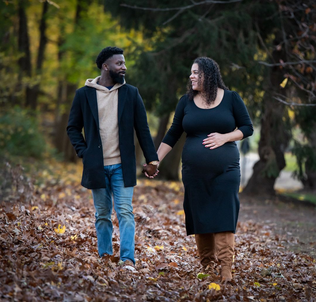 A couple during their maternity shoot holds hands and looks at each other smiling as she holds her belly in Nutley, NJ