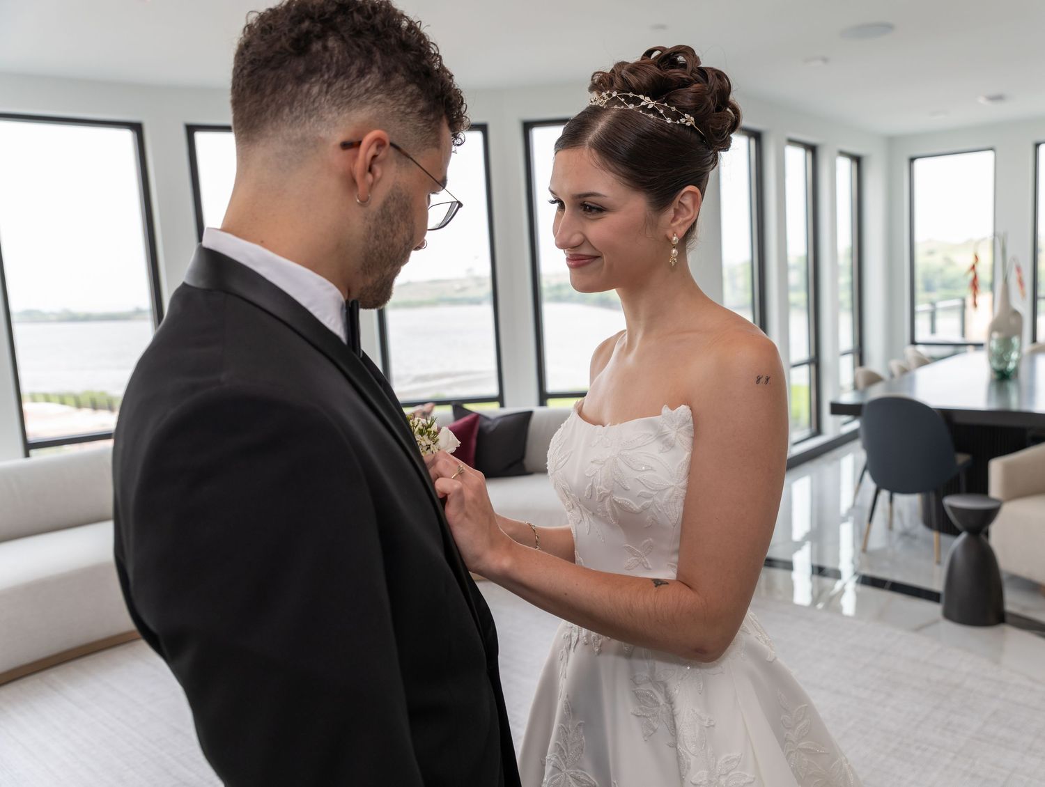 A smiling bride is putting on the groom's button Aire as the groom is looking and smiling at the bride in Bayonne, NJ