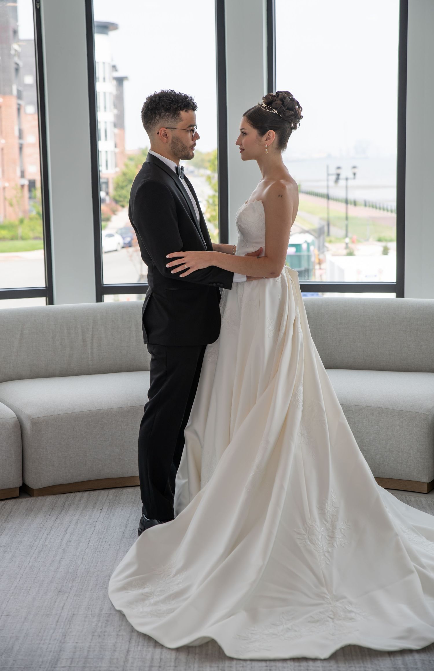 A full body photo of the bride and groom standing towards each other and holding each other and smiling in Bayonne, NJ