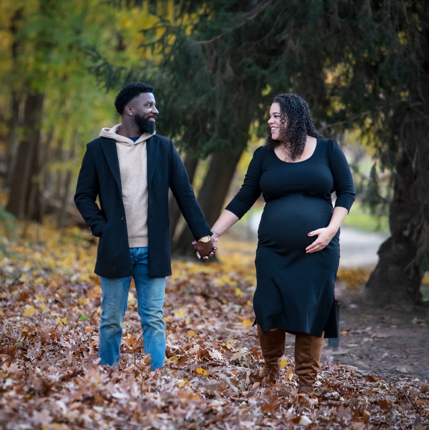 A couple during their maternity shoot holds hands and looks at each other smiling as she holds her belly in Nutley, NJ