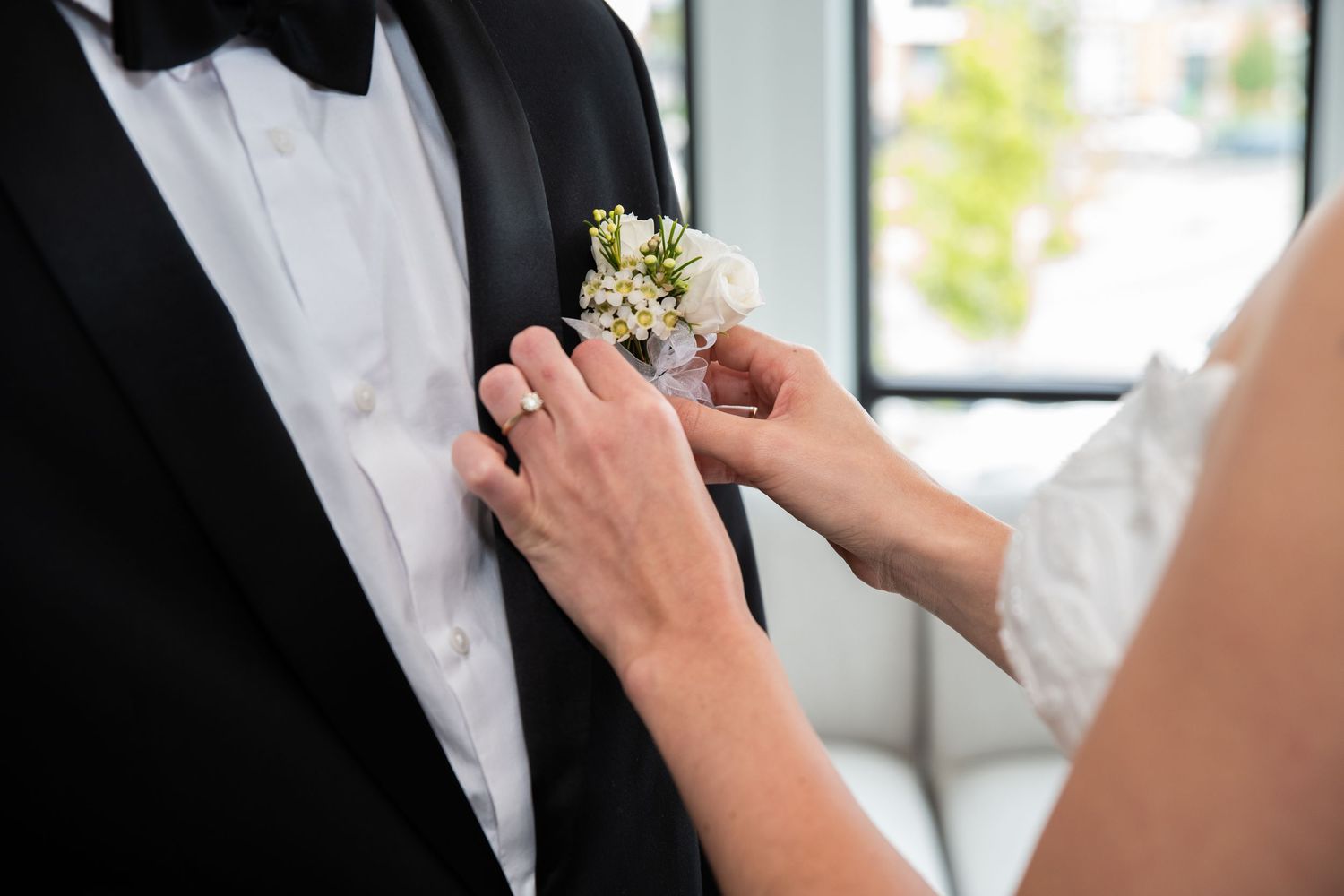 A close up of the bride's hands putting on the button Aire for the groom