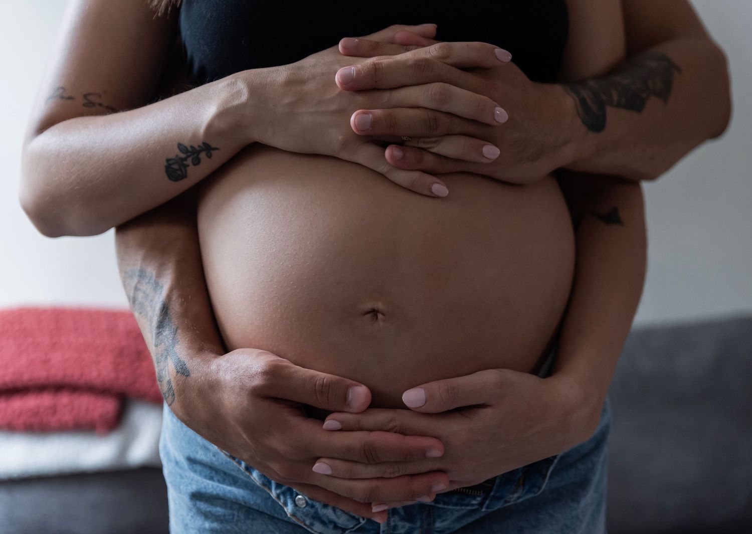 A couple during their maternity photoshoot has their hands intertwined with each other's over the mother's belly in Edgewater, NJ