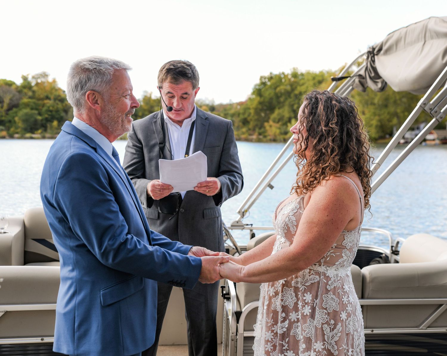 A couple stands face to face at their vow renewal ceremony as the officiant reads the ceremony paper on a lake in Sparta, NJ