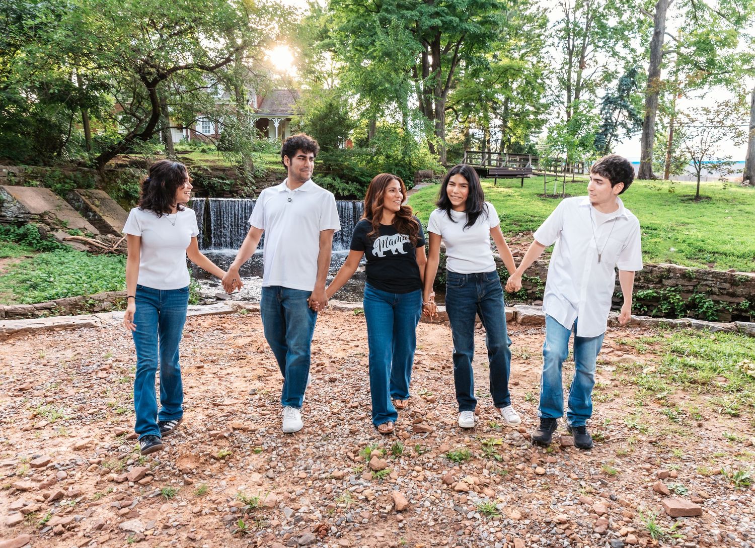 A mom with her 4 kids holds hands, walks towards the camera and smiles at each other during their family photo session in Nutley, NJ