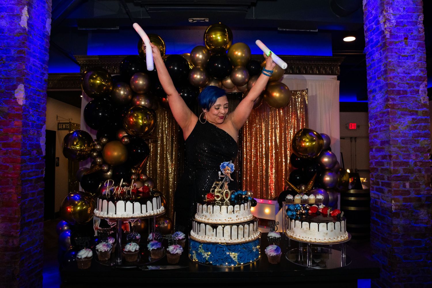 Woman enjoying her 50th birthday party in Rutherford, NJ, being joyful and waving around glow sticks in front of her birthday cake