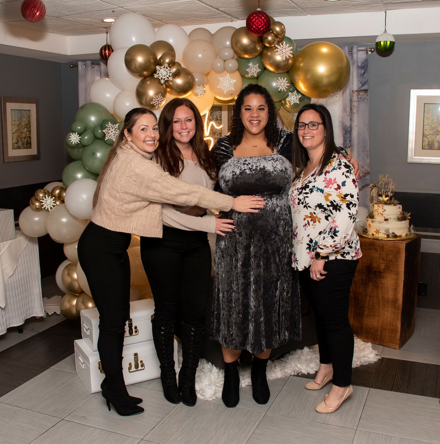 Four women at a baby shower in New Jersey, posing for the camera and joyfully holding the pregnant belly of the mother to be