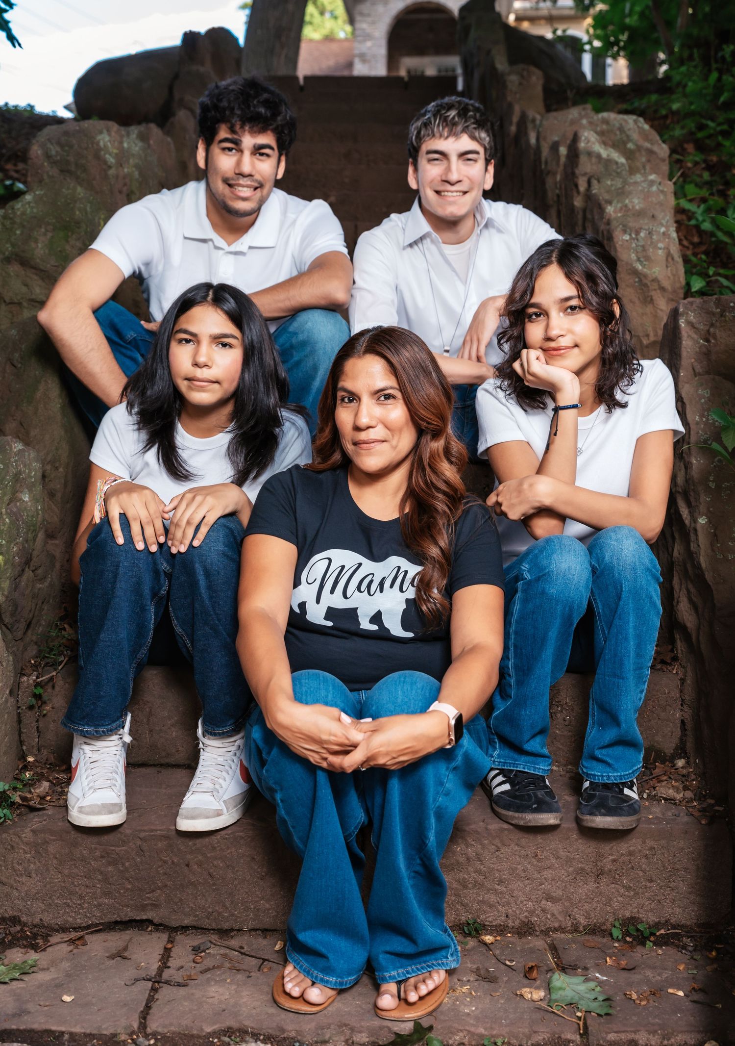 A mom with her 4 kids sits on steps looking at the camera and smiling during their family photo session in Nutley, NJ