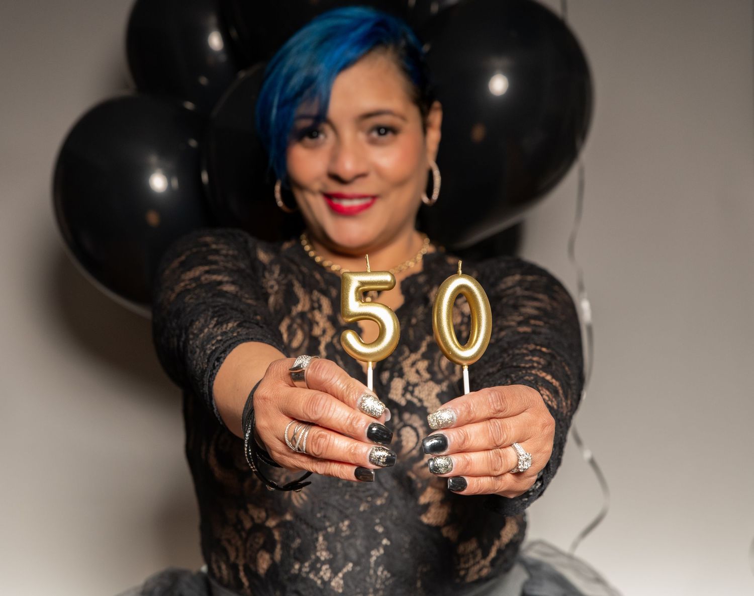 A portrait of a woman for her 50th birthday photo shoot holding up candles that say 50 with balloons in the background in Woodridge, NJ