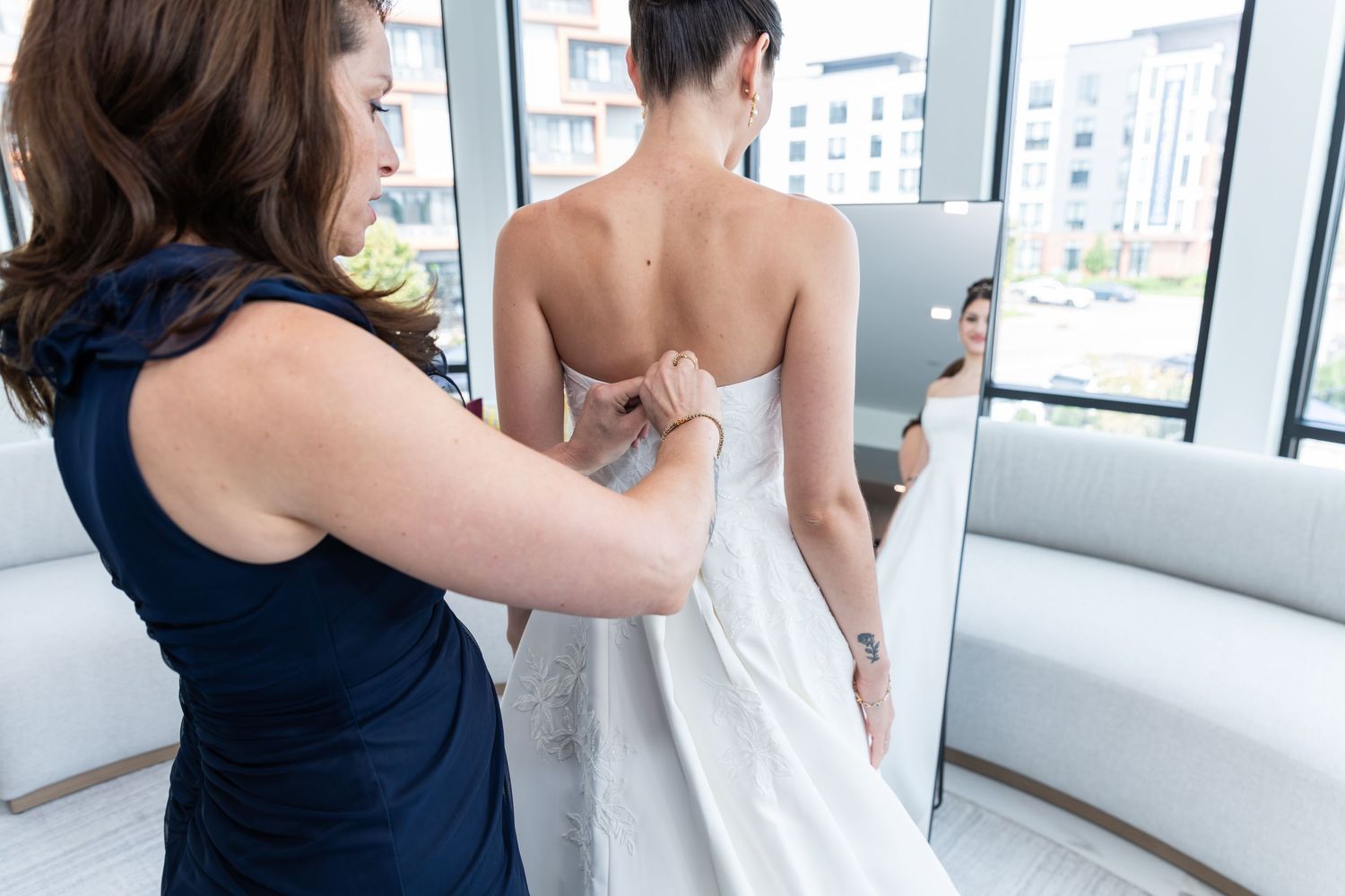 A photo of the bride with her mother as she is helping to button up her wedding dress as she is looking in the mirror in Bayonne, NJ