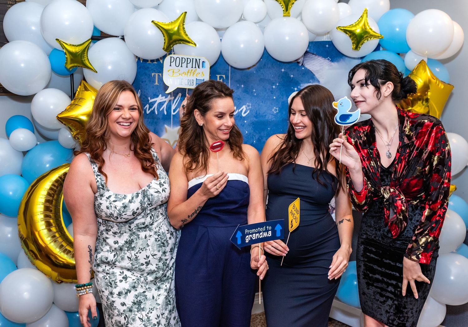 Four women celebrating a baby shower in Bridgewater, NJ, laughing and posing with funny photo props