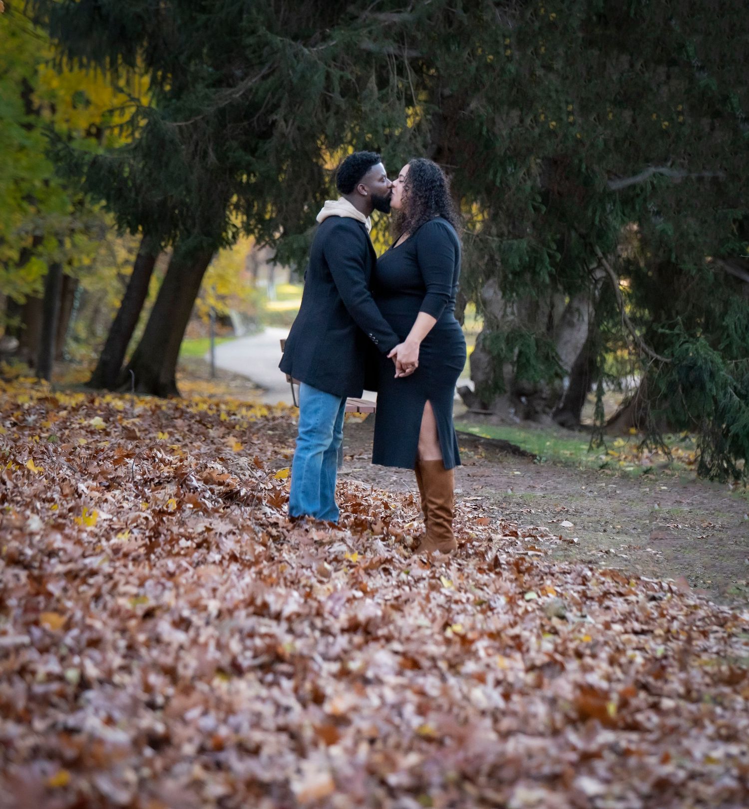A couple during their maternity shoot holds hands and is facing each other while kissing in Nutley, NJ