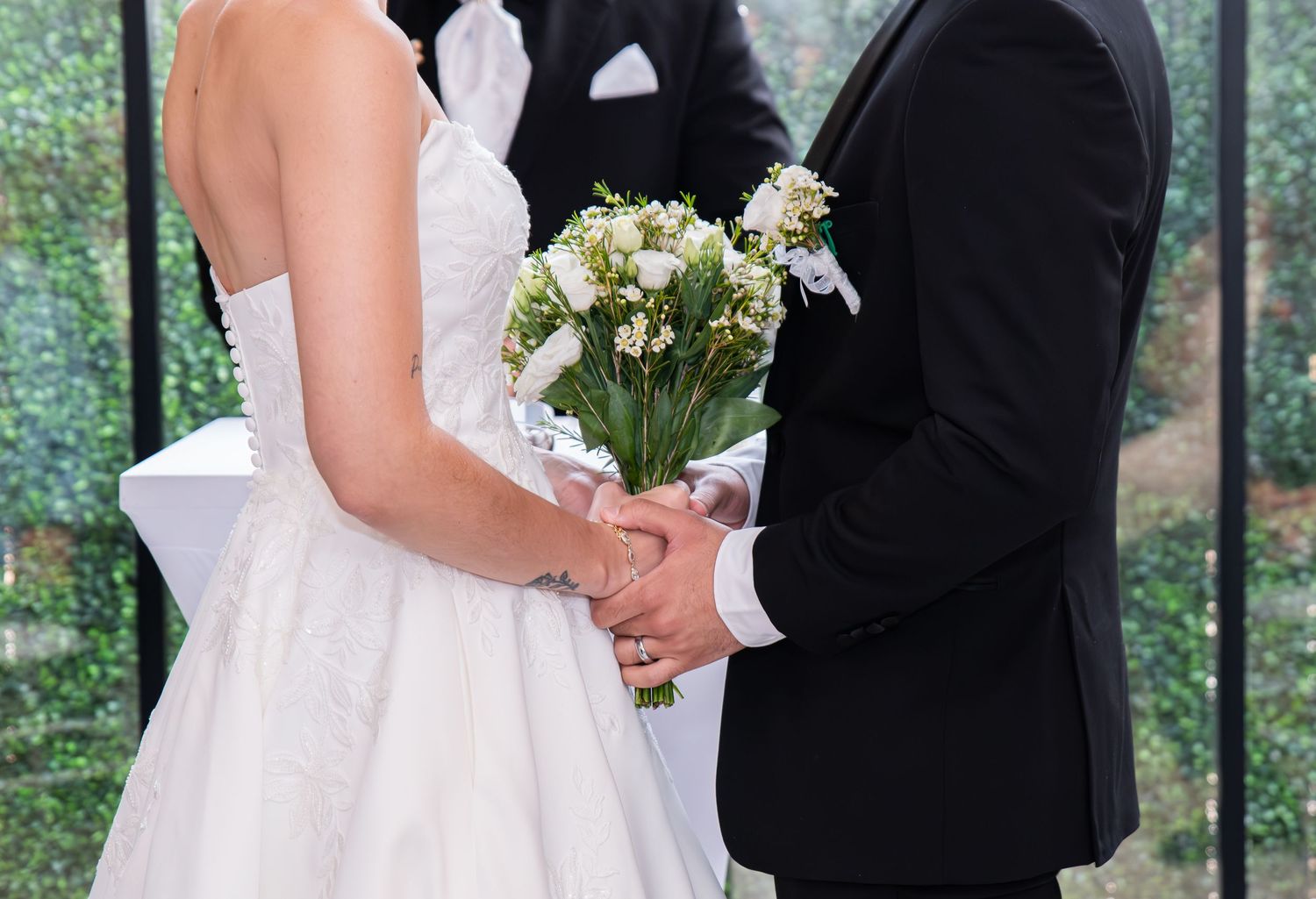 A close-up photo of the bride and groom's hands holding the bride's bouquet together in Bayonne, NJ