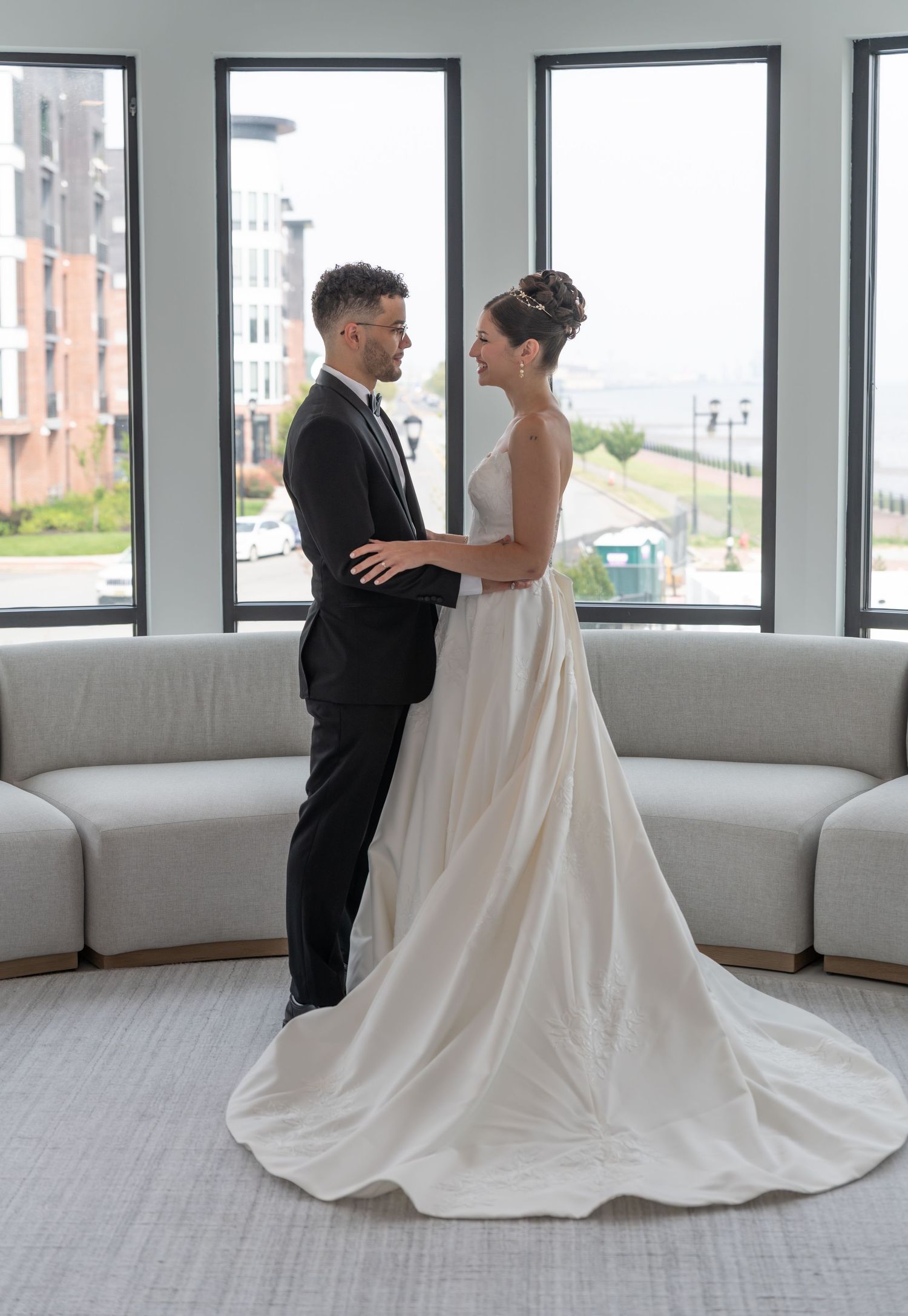 A full body photo of the bride and groom standing towards each other and holding each other and smiling in Bayonne, NJ