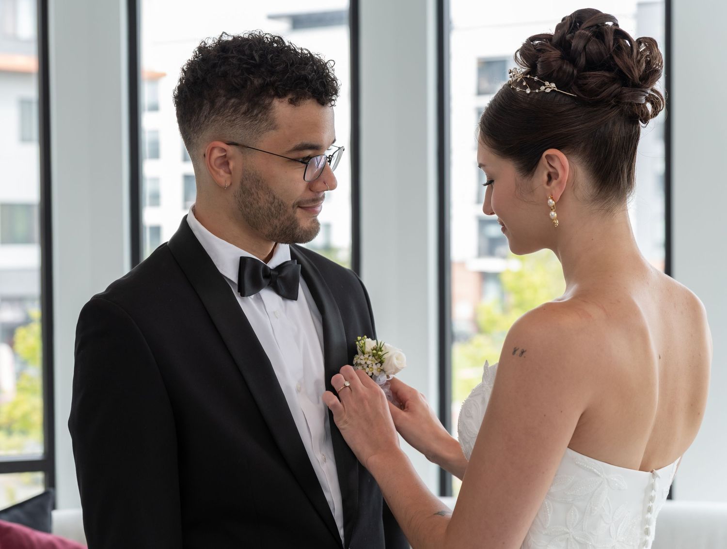 A bride is putting on the groom's button Aire as the groom is looking and smiling at the bride in Bayonne, NJ