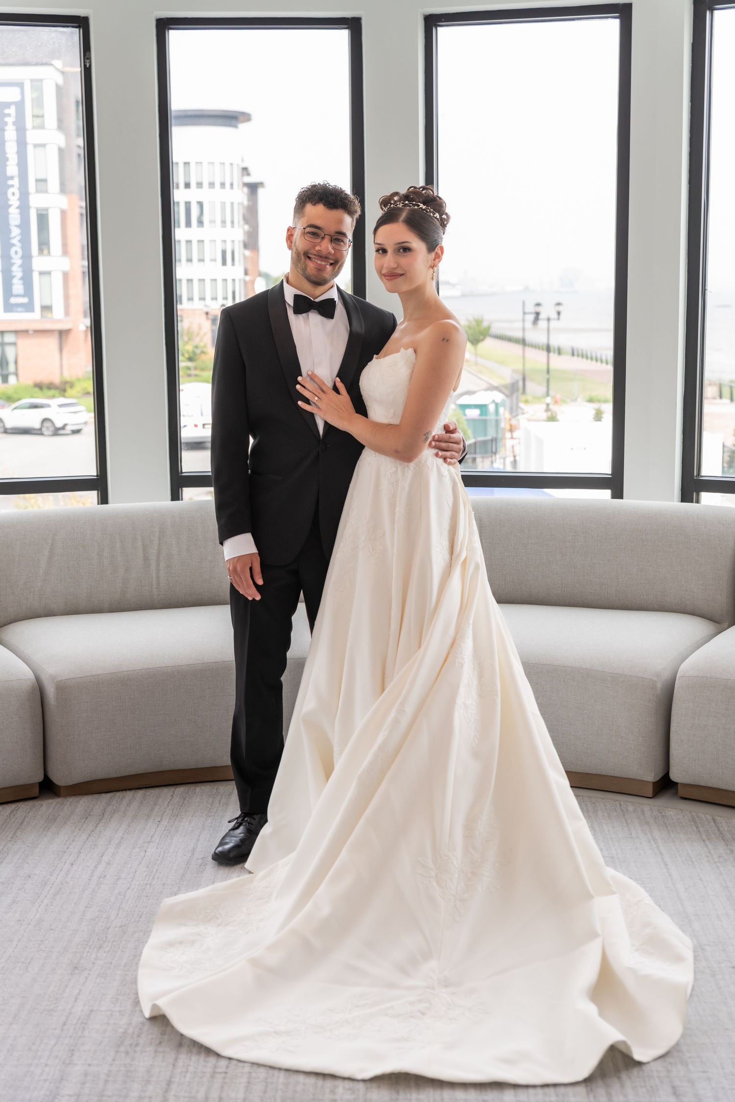 A full body photo of the bride and groom standing towards the camera and holding each other and smiling in Bayonne, NJ