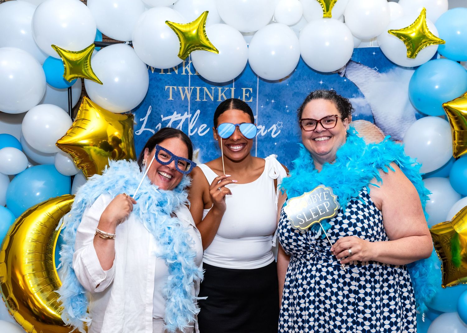 Three women celebrating at a baby shower in Bridgewater, NJ, laughing and posing with funny props, capturing joyful, candid moments