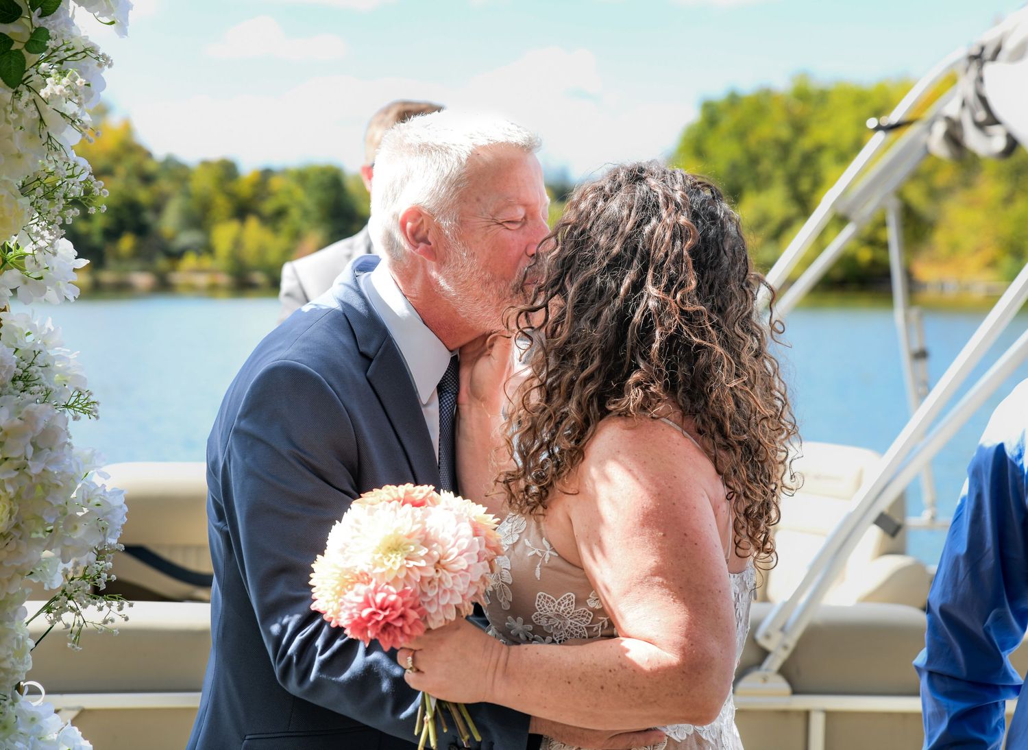 A couple kisses on a boat dock at their vow renewal ceremony on a lake in Sparta, NJ