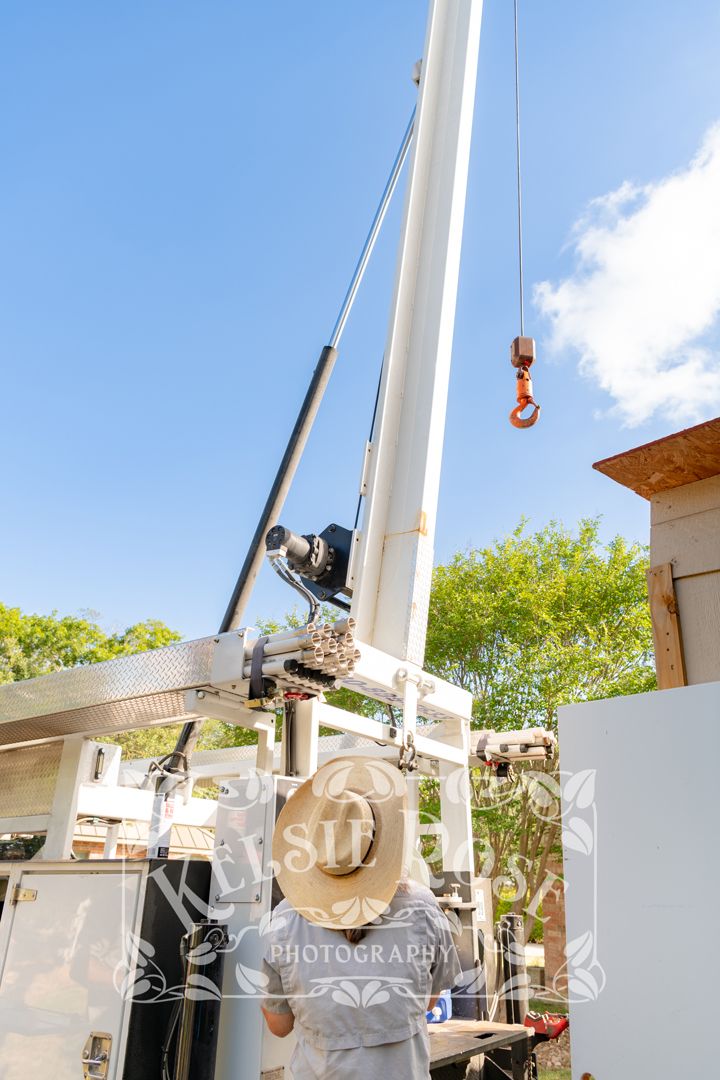 Worker in straw hat operating white crane boom against clear blue sky.