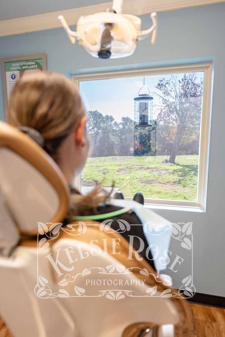 Dental patient in chair enjoying view of bird feeder and yard through treatment room window.