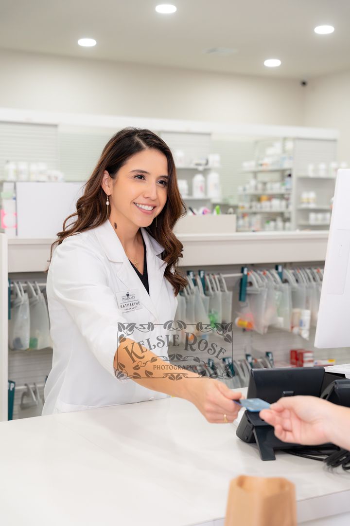 Smiling female pharmacist processing a credit card payment for a customer at pharmacy checkout counter.