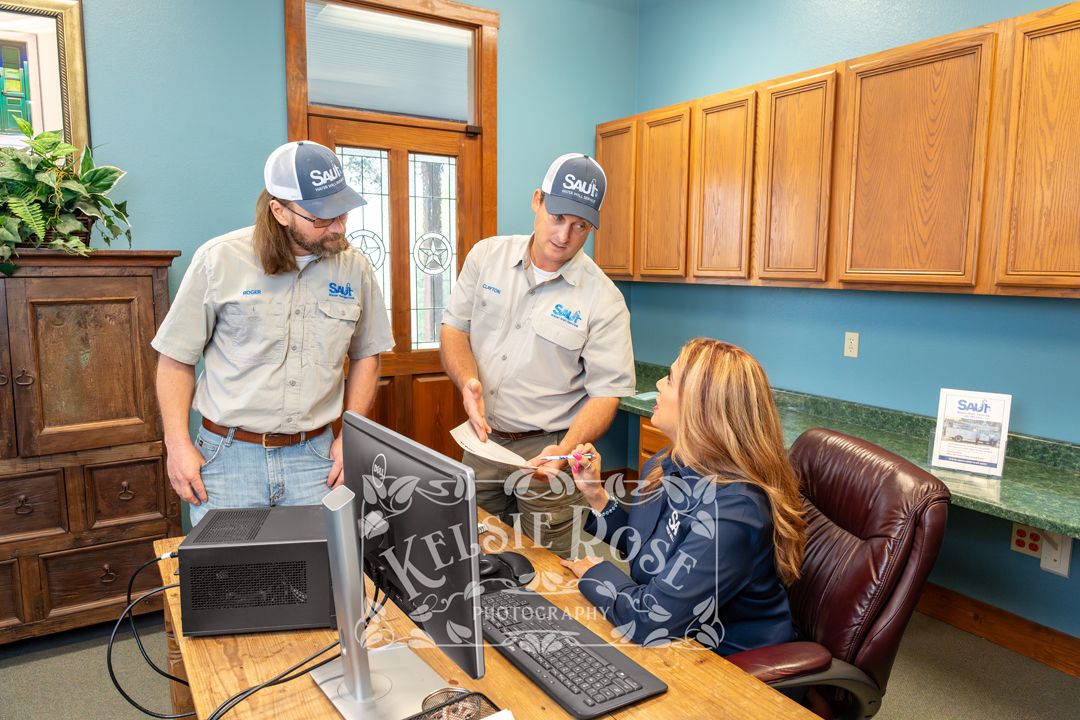 Two Saul Water Well Service technicians consulting with female office staff at a desk in an office.