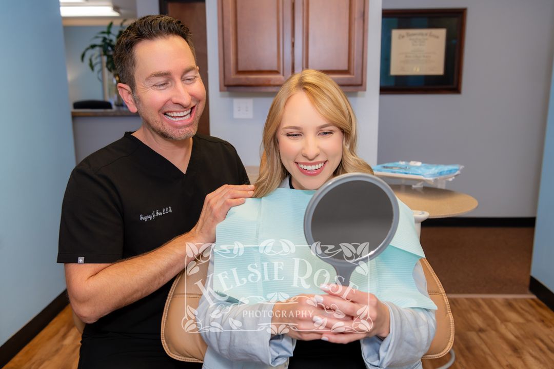 Dentist showing a happy female patient her smile results using a handheld mirror in dental office.