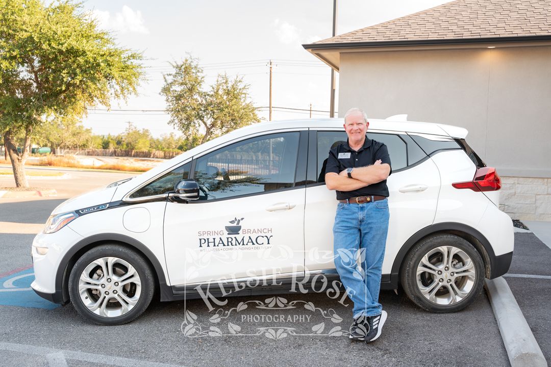Spring Branch Pharmacy delivery driver standing beside branded white electric vehicle outdoors.