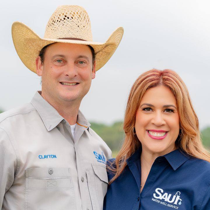Businessman in cowboy hat and woman in matching company shirts smile together outdoors for professional portrait.