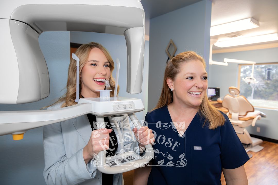 Dental assistant helping smiling patient use panoramic dental X-ray machine.