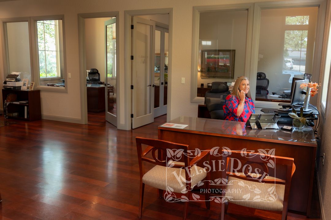 Woman sitting at a wooden reception desk in an elegant office with cherry hardwood floors and French doors.
