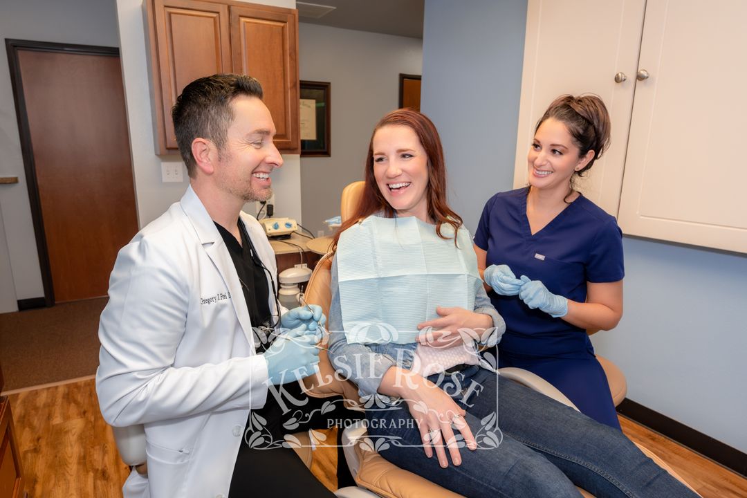 Smiling dentist and dental assistant consulting with a happy female patient in a treatment chair.