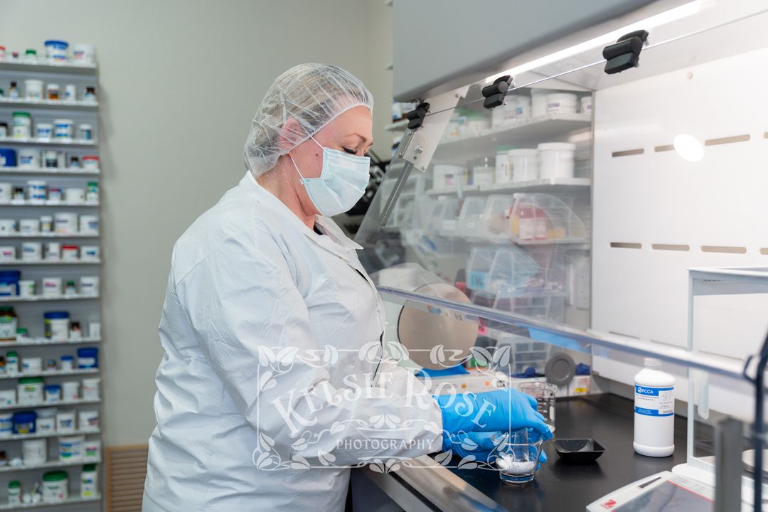 Pharmacist in white coat and mask carefully compounding medication at a laboratory workstation.