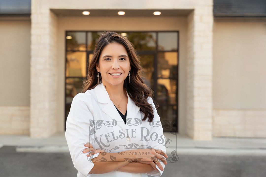 Smiling female pharmacist in white coat standing with arms crossed outside pharmacy entrance.