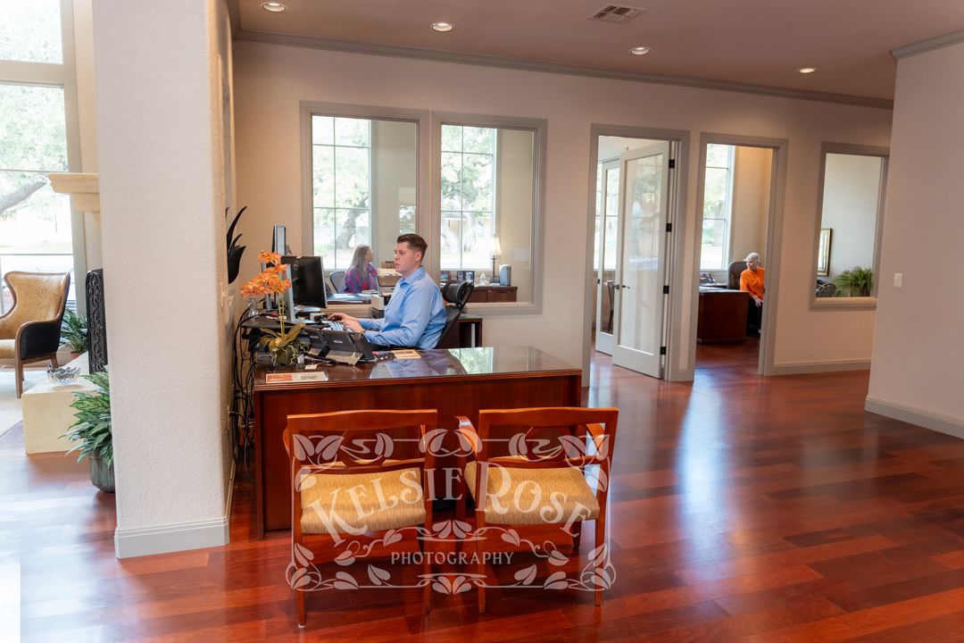 Man working at an ornate wooden reception desk in a bright office with cherry hardwood floors.