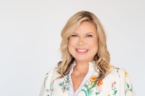 Smiling blonde businesswoman in a floral dress poses for a professional headshot against a white background.