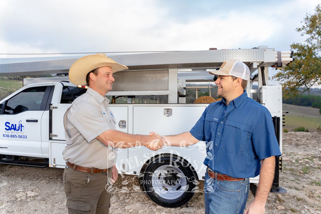 Two men shaking hands in front of a company service truck in an outdoor rural setting in Texas.