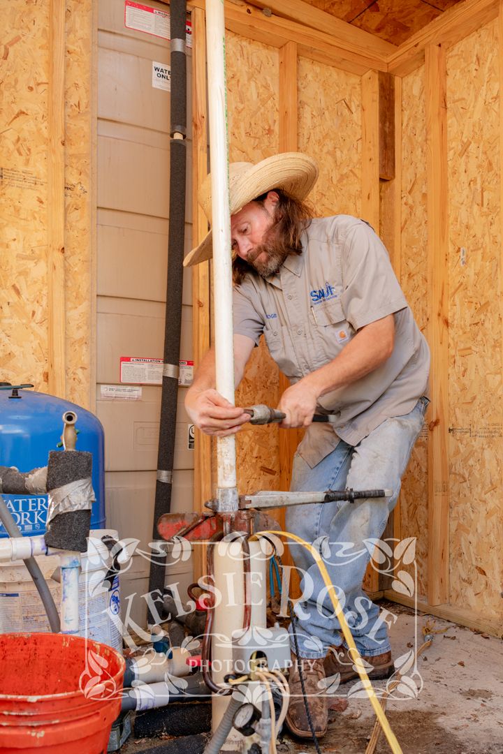 Bearded worker in straw hat pulling well pump pipe inside wooden well building.