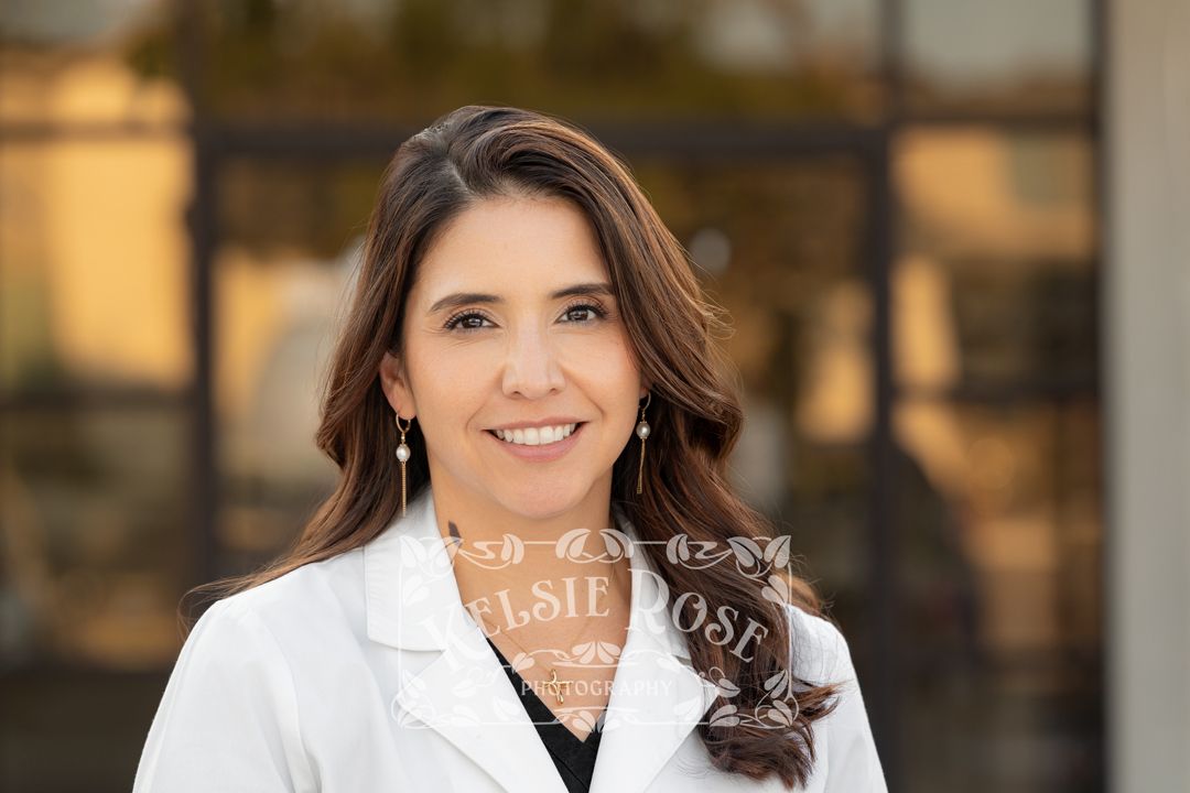 Headshot of female healthcare professional in white lab coat posing outdoors in front of a modern building.