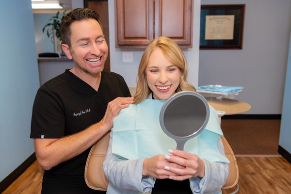 Dentist and smiling female patient admiring her bright new smile in a hand mirror at a dental office.