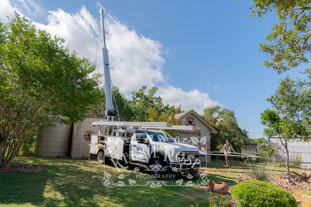 Water well service comapny truck with extended crane boom in residential backyard on a partly cloudy day.