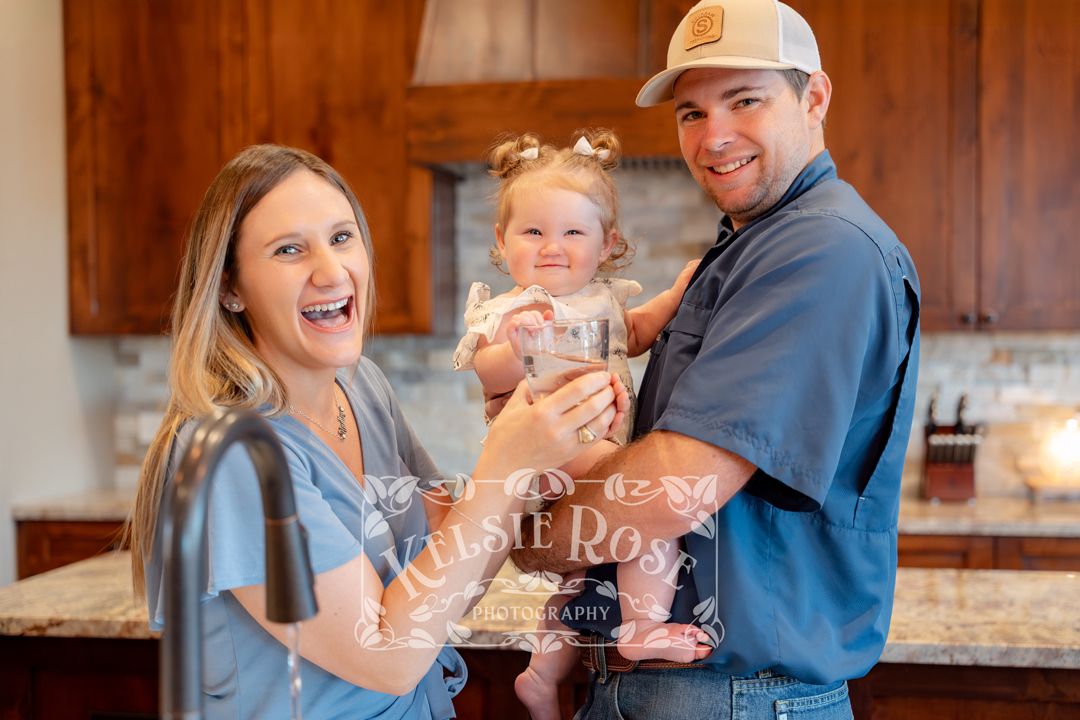 Happy young family with toddler celebrating with glass of clean water in modern kitchen.