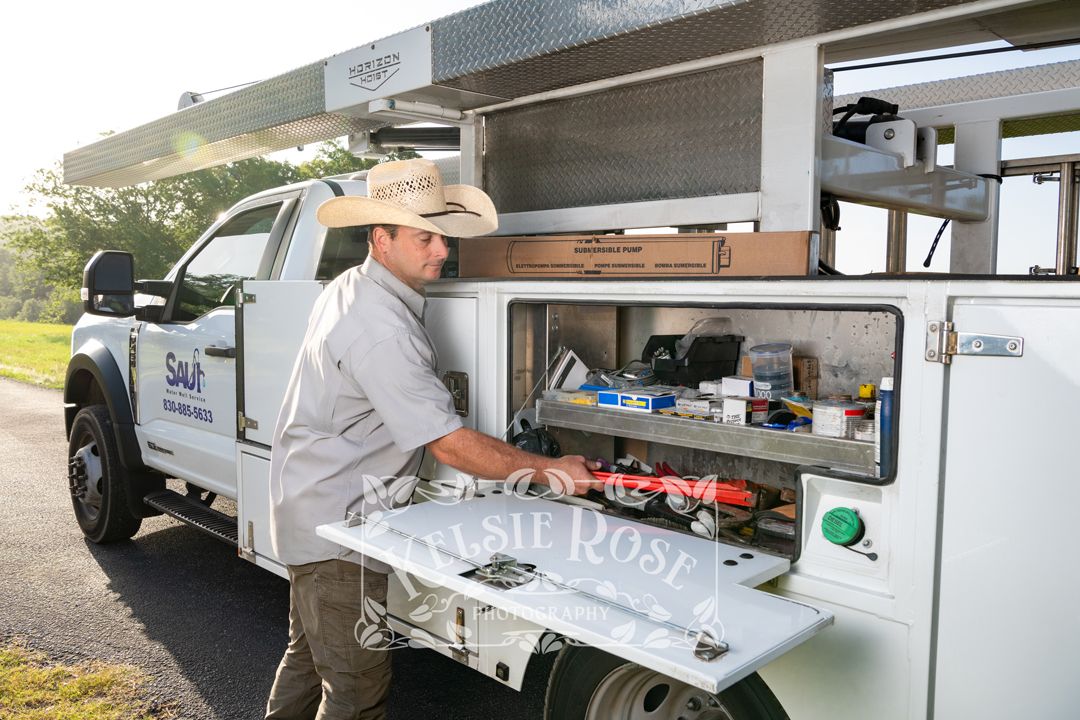 Male technician in cowboy hat accessing equipment storage from water well service company truck.