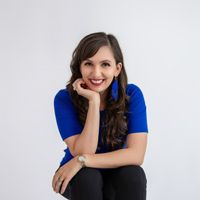 Professional headshot of a smiling brunette photographer in a blue top seated against a white background.