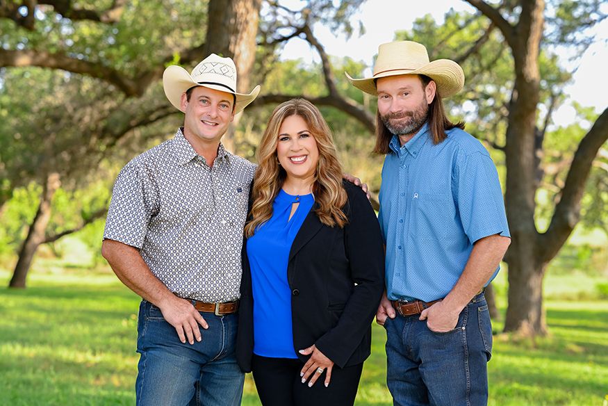 Three smiling people pose outdoors in a lush green ranch setting in Texas.