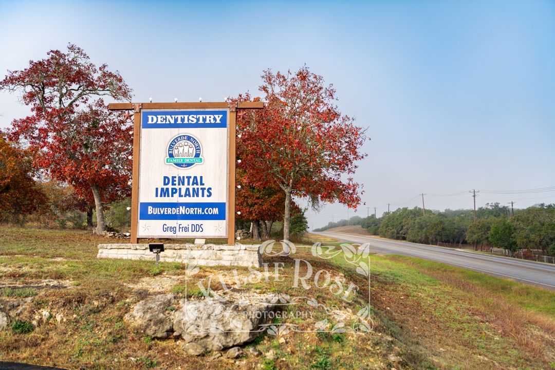 Close-up of a sign for a dentistry practice with red autumn trees along a Texas road.