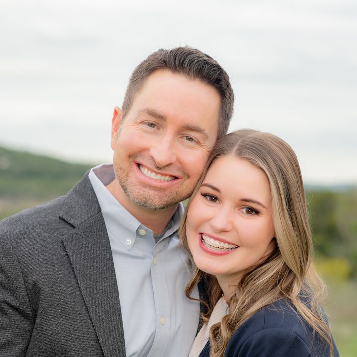 Married couple shares a close embrace in an outdoor portrait with scenic green hills behind them.